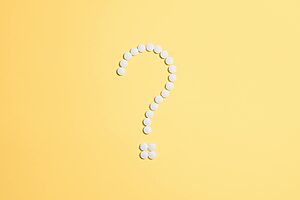 White pills arranged into a question mark shape on a vibrant yellow background.